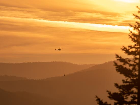 Orange smokey haze over mountains with helicopter circling above. 
