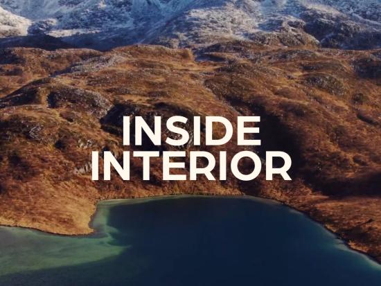 White text Inside Interior over a landscape of snow capped mountains and a lake. 