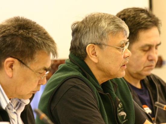 Closeup of 3 men; the one in the center is speaking into a microphone