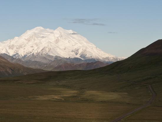 Snow covered mountain peak behind a green valley in the crisp morning light. 