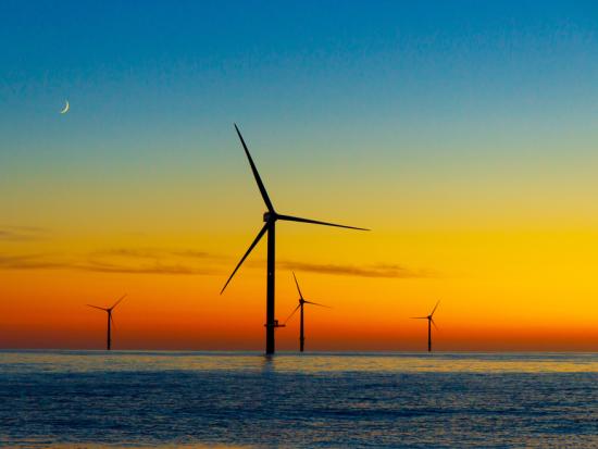 Offshore wind turbines with a brightly colored sunset.