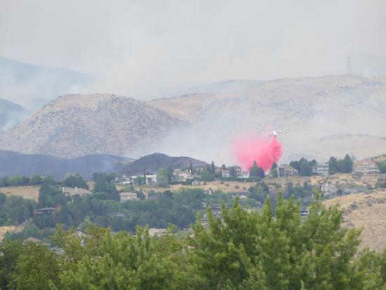 A plane drops a red plume over buildings with smoke in the backgound