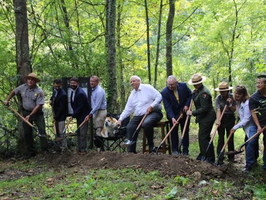a line of people tossing dirt from shovels at a trailhead