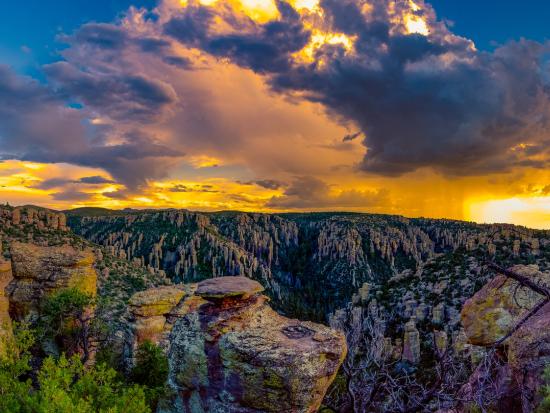 Rock pinnacles in the foreground with blue sky and a dramatic rainfall in front of sunlight.
