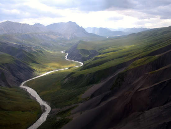 Green mountains rolling into river. Cloudy Skies. 