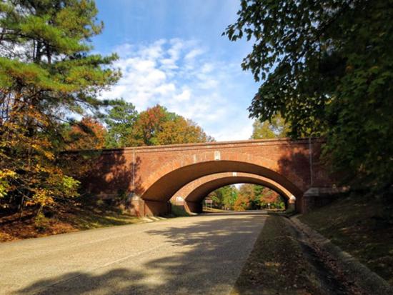 Paved road leading to two red stone bridges with trees on either side and a blue sky