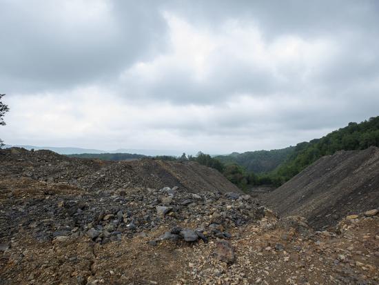 A view of an abandoned coal mine land with a large pile of dirt and rocks covering the ground and trees and hills in the background