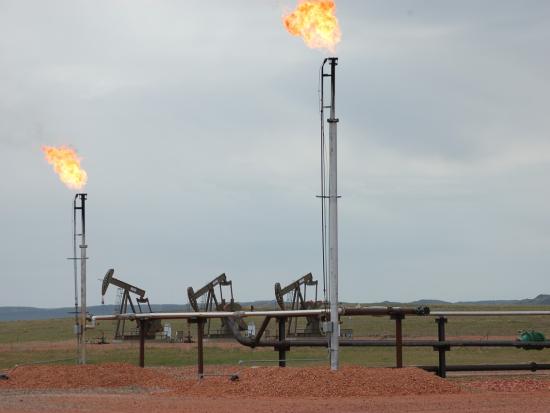 Three oil pumps with two flare stacks and a mountain range in the far distance