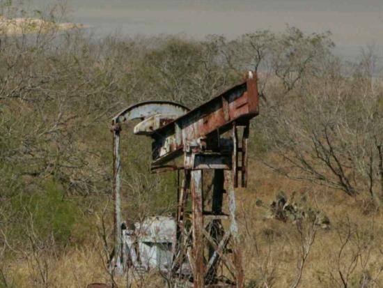 An orphan well with rusted equipment sitting above it amid grass and brush