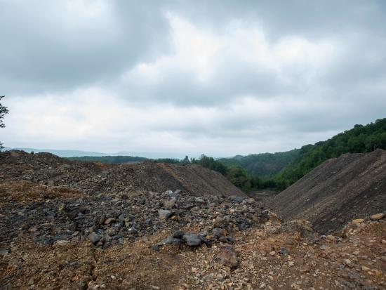 Large mounds of dirt and rocks sit in piles with trees in the background