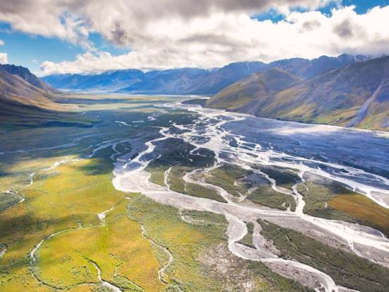 Aerial view of green mountains surrounding a river valley. Cloudy sky sits low over the mountains. 