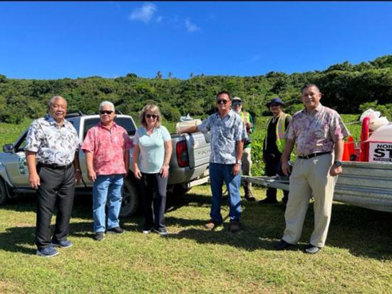 Asst. Sec Cantor standing with group in front of two trucks at infested site on Saipan.