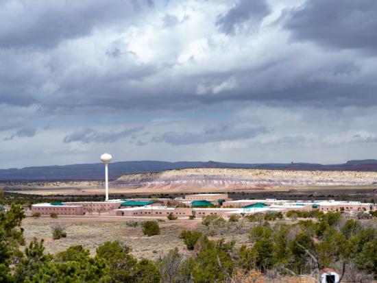 Distant view of large school building complex surrounded by desert landscape and dark cloudy sky. 