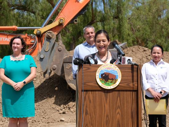 Secretary Haaland speaking at DOI podium in front of a construction site. 
