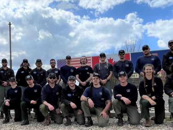 A National Park Service hotshot crew stands in a group before US and Canada flags.