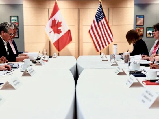 Secretary Haaland and other leaders sit at tables with the American and Canadian flags in the backdrop.