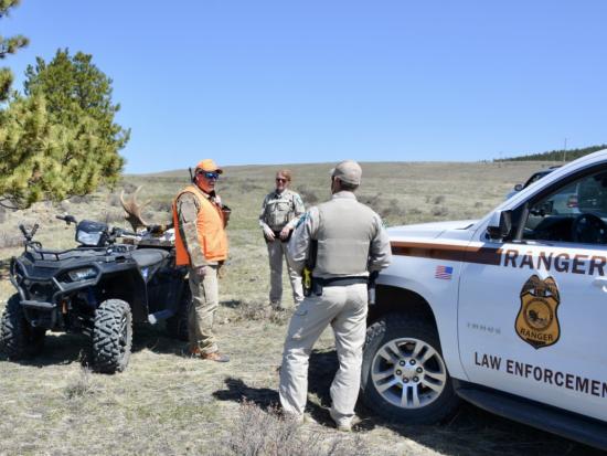 Two Department Law Enforcement Rangers speaking to a hunter in orange vest. 