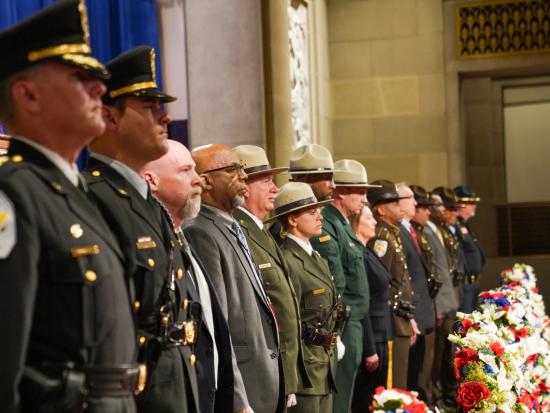 Fifteen enforcement officers stand in a row at the Peace Officers Memorial