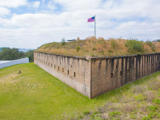 A flag flies over a masonry fort topped by grass at at Fort Barrancas.
