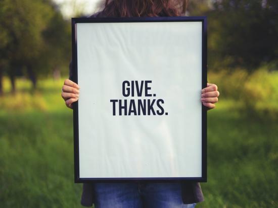 Person holding a sign in a field that says "Give. Thanks."