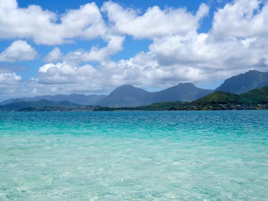 Clear-blue waters reflecting cloudy sky and mountains in the background. 