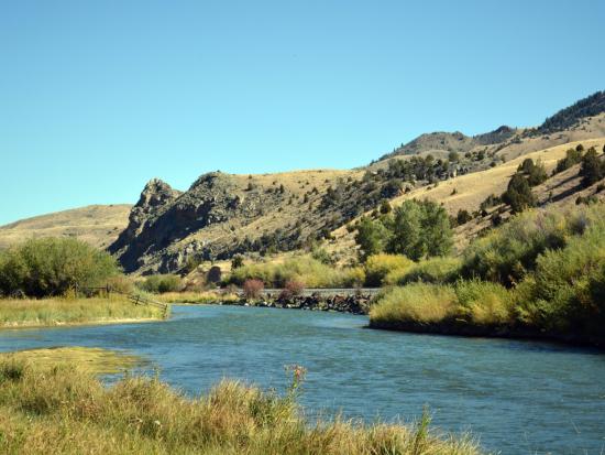River cuts through rolling hills under a blue sky.