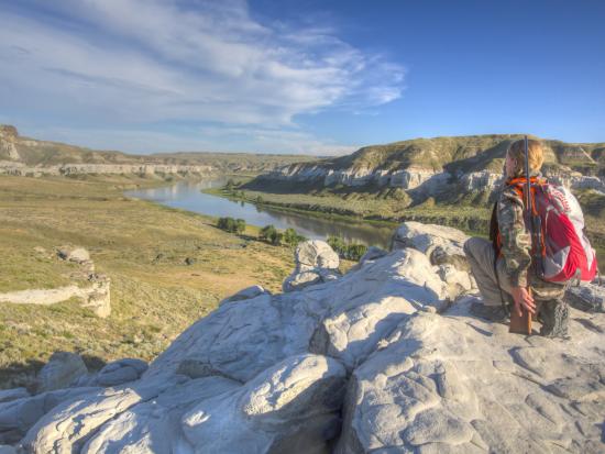 Hunter kneels on a rock overlooking a river and valley below.