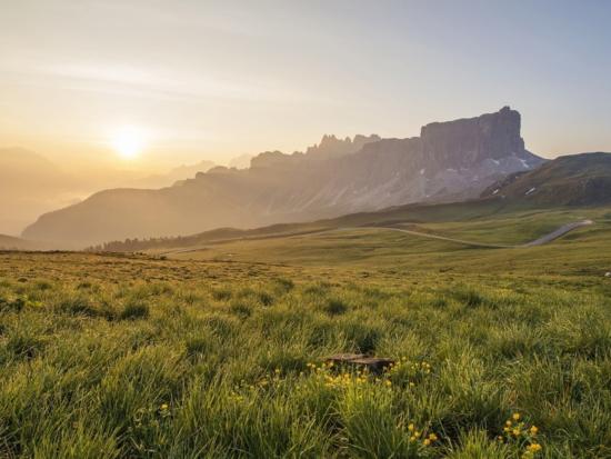Image of green field with sunrise and rock formations in background.