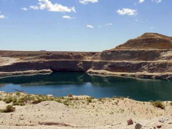 Image shows a body of water surrounded by mountain like hills in a desert under a cloudy blue sky