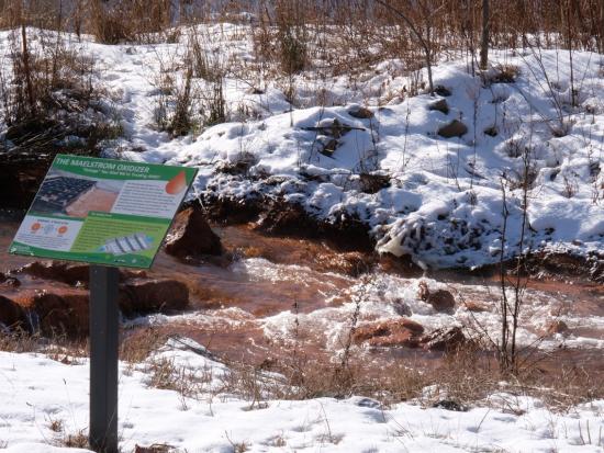 Water with orange pollution in a river flows past a bank covered in snow