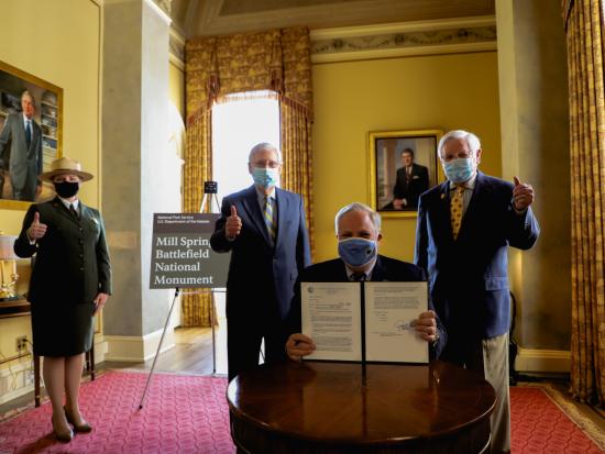 Secretary Bernhardt sits at a small table in a fancy room holding up a folder with a signed paper inside.