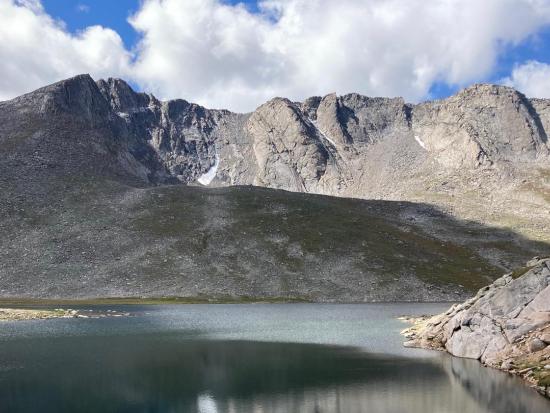 Rocky mountain peak surrounded by cloudy sky and wilderness area with a lake. 