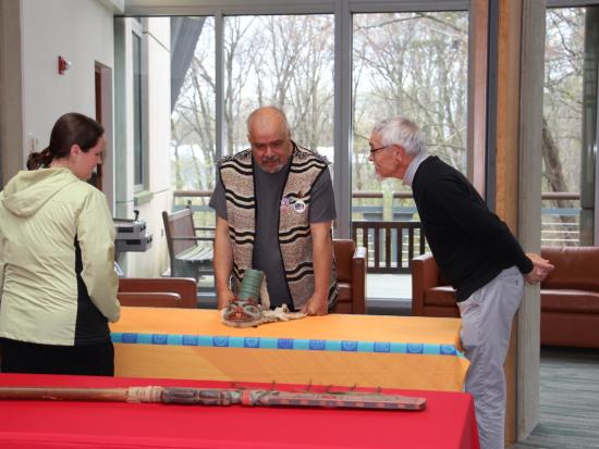 Three people stand around a table and look at a Tlingit clan hat