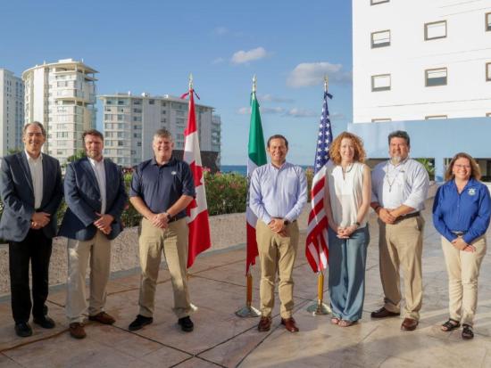 Seven people stand together with the Canada, Mexico and U.S. flags behind them