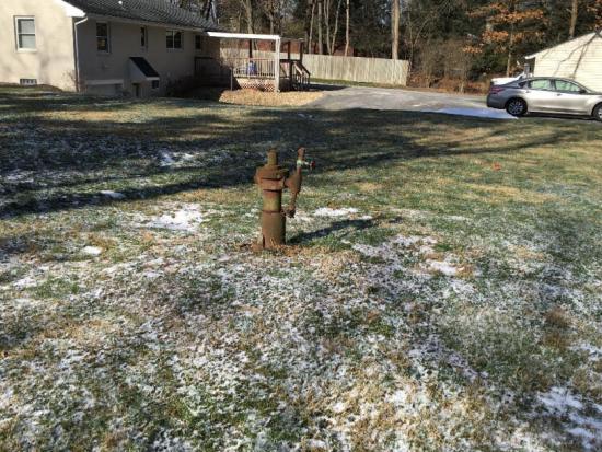 An orphan well with rusted equipment above it in the yard of a home
