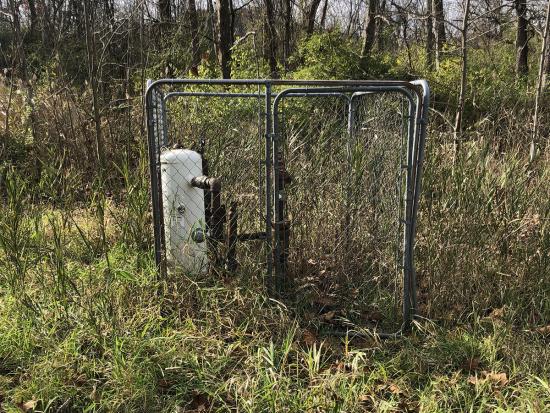 A caged off orphan well surrounded by brush