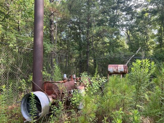 Orphaned oil and gas well enclosed in a fenced in area in a forest.