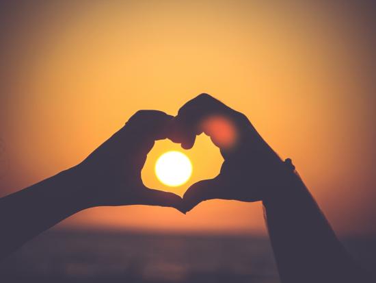 Picture of two hands making a heart at sunset