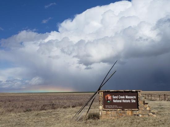 The Sand Creek Massacre National Historic Site sign in a field with white clouds in the background