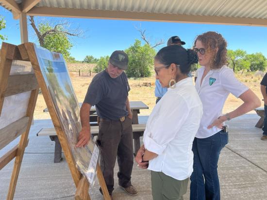 Secretary Haaland and two others in BLM shirts view a map outdoors.