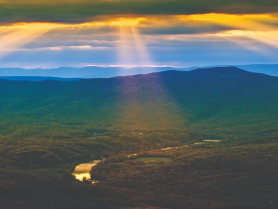 Sun beams break through clouds to shine on a lush mountain valley.