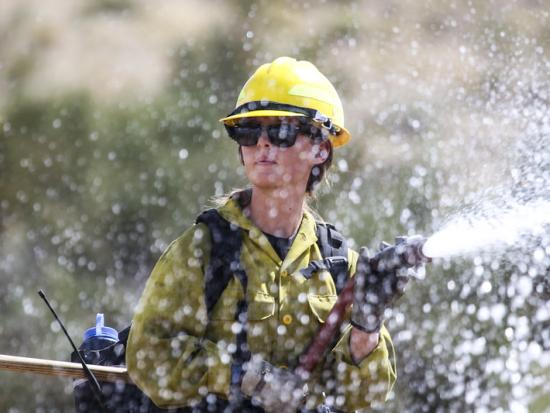 A Wildland firefighter sprays water out of a hose