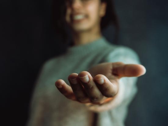 A smiling woman extends her hand in a gesture of support. Photo by Ave through Adobe Stock.