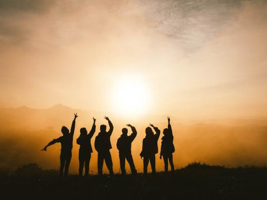 Six people silhouetted against a sunrise with mist