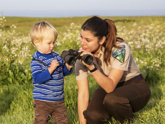 A BLM ranger helps a child look through binoculars