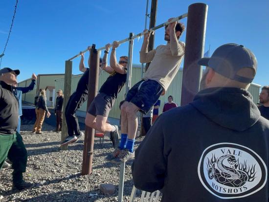 Three wildland firefighters do pull ups on a pull up bar.  
