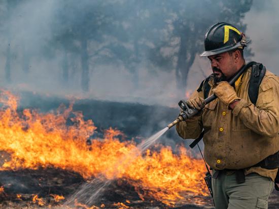 A wildland firefighter sprays water on a fire. By Colby Neal, BLM.