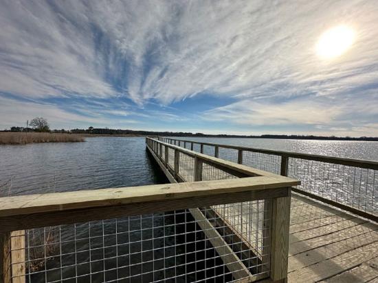 A brown boardwalk sits in the middle of a large body of water on a sunny day. 