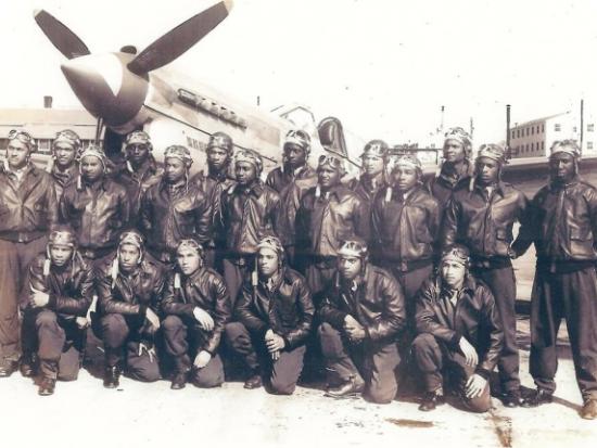 Tuskegee Airmen graduates from advanced single-engine pilot training pose in two lines in front of a World War 2 fighter plane.
