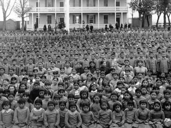 Historical photo of Indigenous children gathered outside a boarding school  